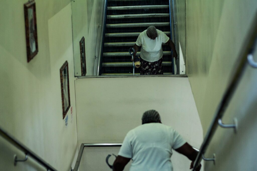 Ältere Frau mit Gehstock geht eine schmale Treppe mit Handlauf hinunter